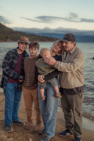 A family stands together on a beach at sunset with mountains and water in the background.