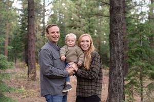 A happy family shares warm embraces while posing outdoors in a pine forest setting during an autumn photoshoot.