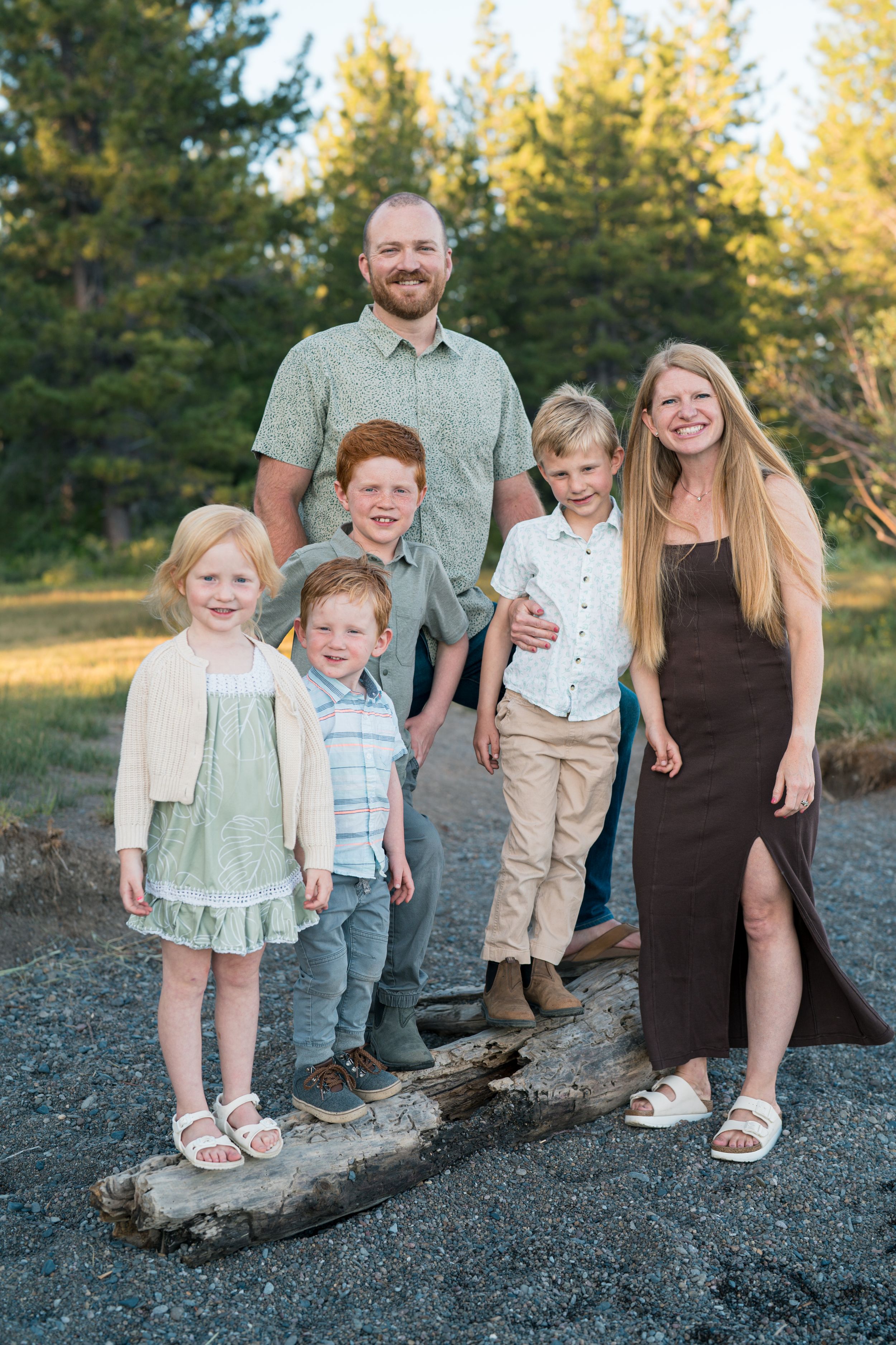 A family of five stands together on a rocky path with evergreen trees in the background during golden hour.