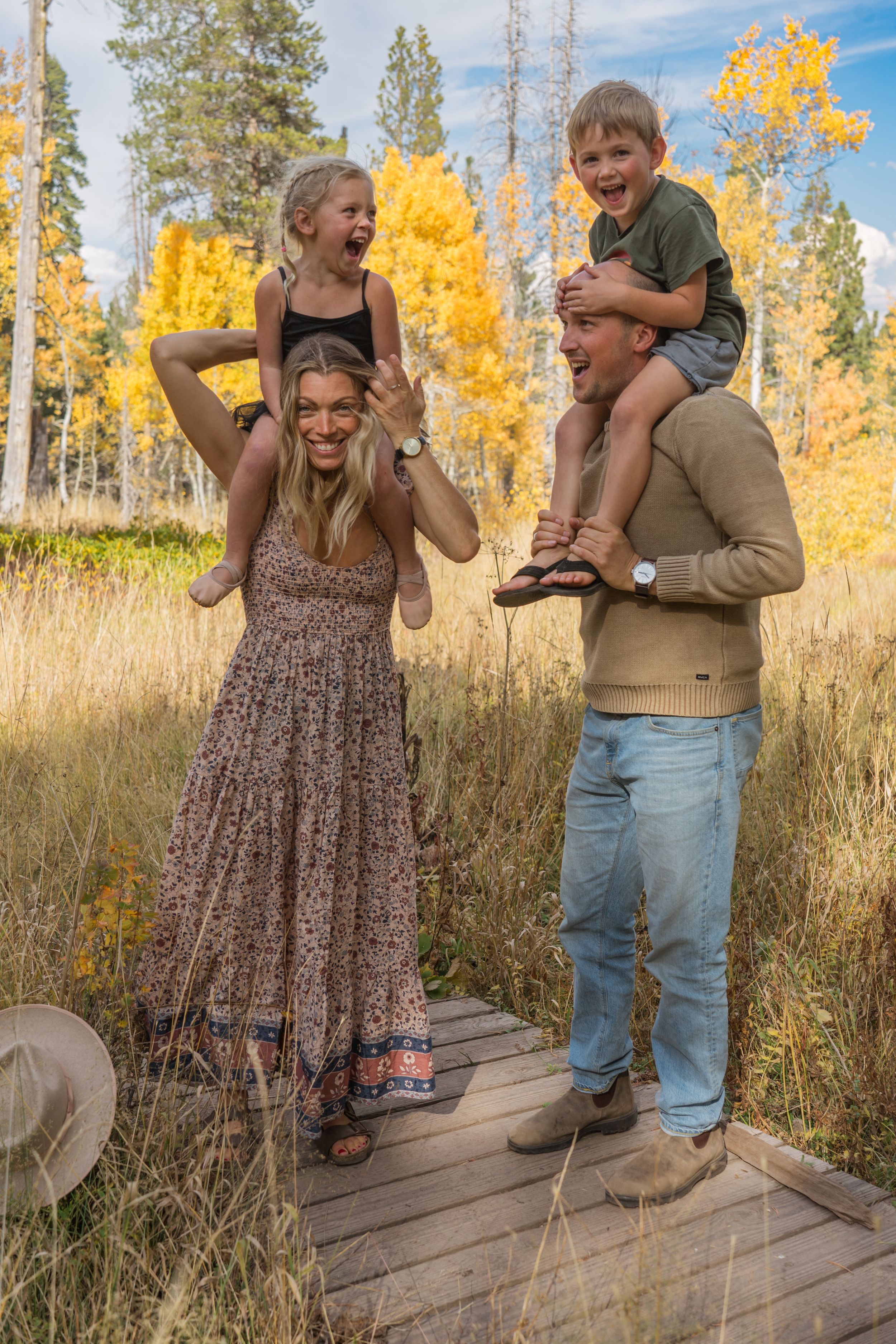 A couple shares a playful moment laughing together on a wooden deck with autumn foliage in the background.