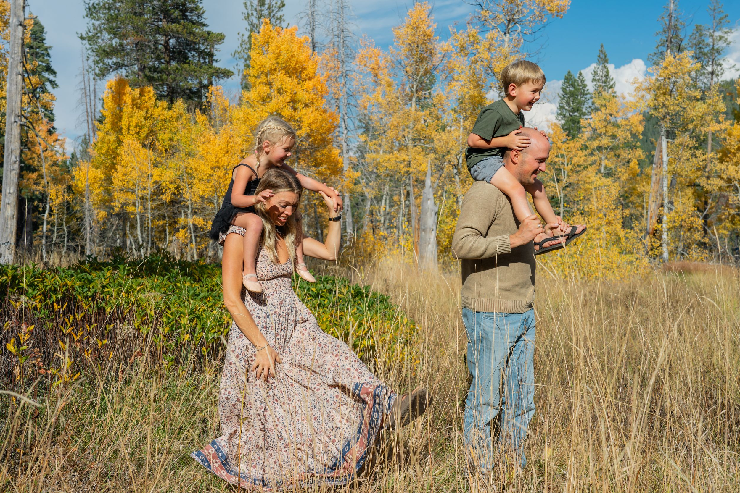A family enjoys an autumn day together in a field surrounded by golden aspen trees and tall grass.