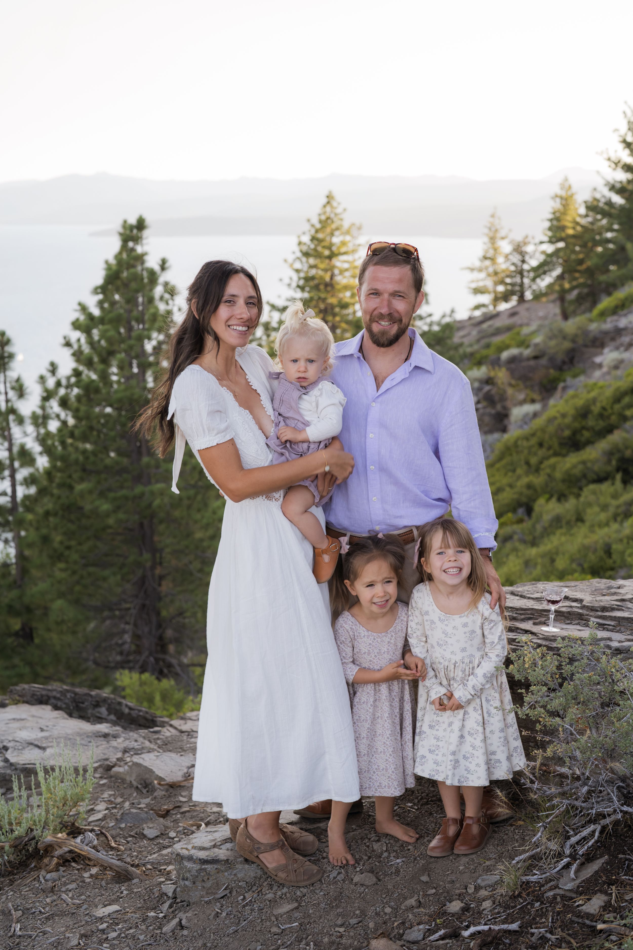 Family in white and purple outfits poses together on rocky mountain terrain at sunset.