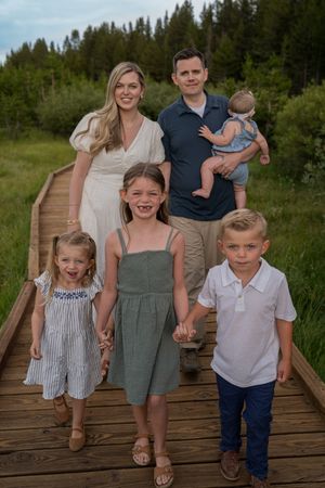 A family poses together on a wooden boardwalk surrounded by evergreen trees and natural scenery.
