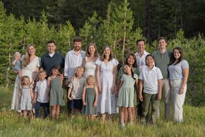A group of people wearing coordinating white and gray outfits pose together outdoors in a natural setting.