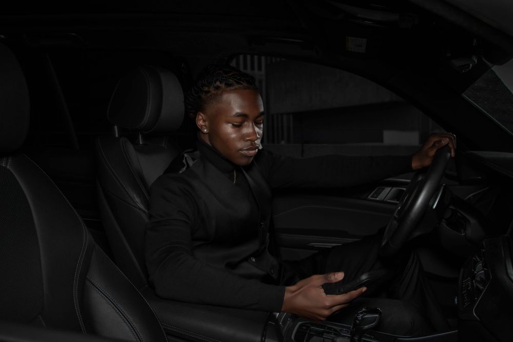 Person in a black shirt sits in the driver's seat of a dark vehicle interior at night.