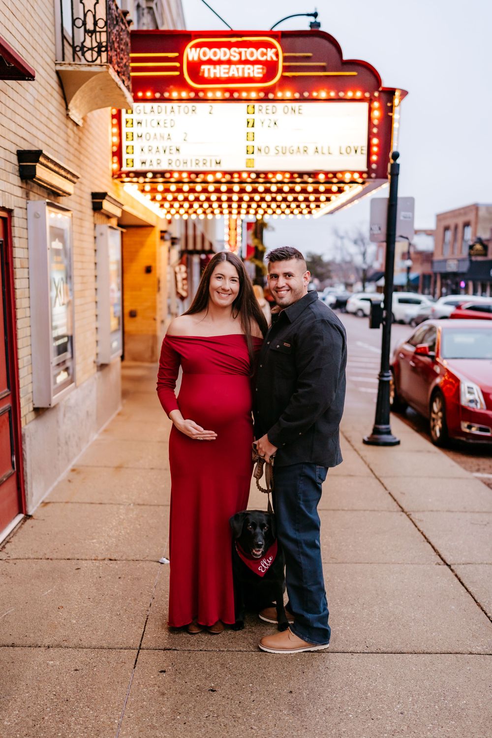 A couple poses outside the illuminated Woodstock Theatre marquee at dusk on a city sidewalk.