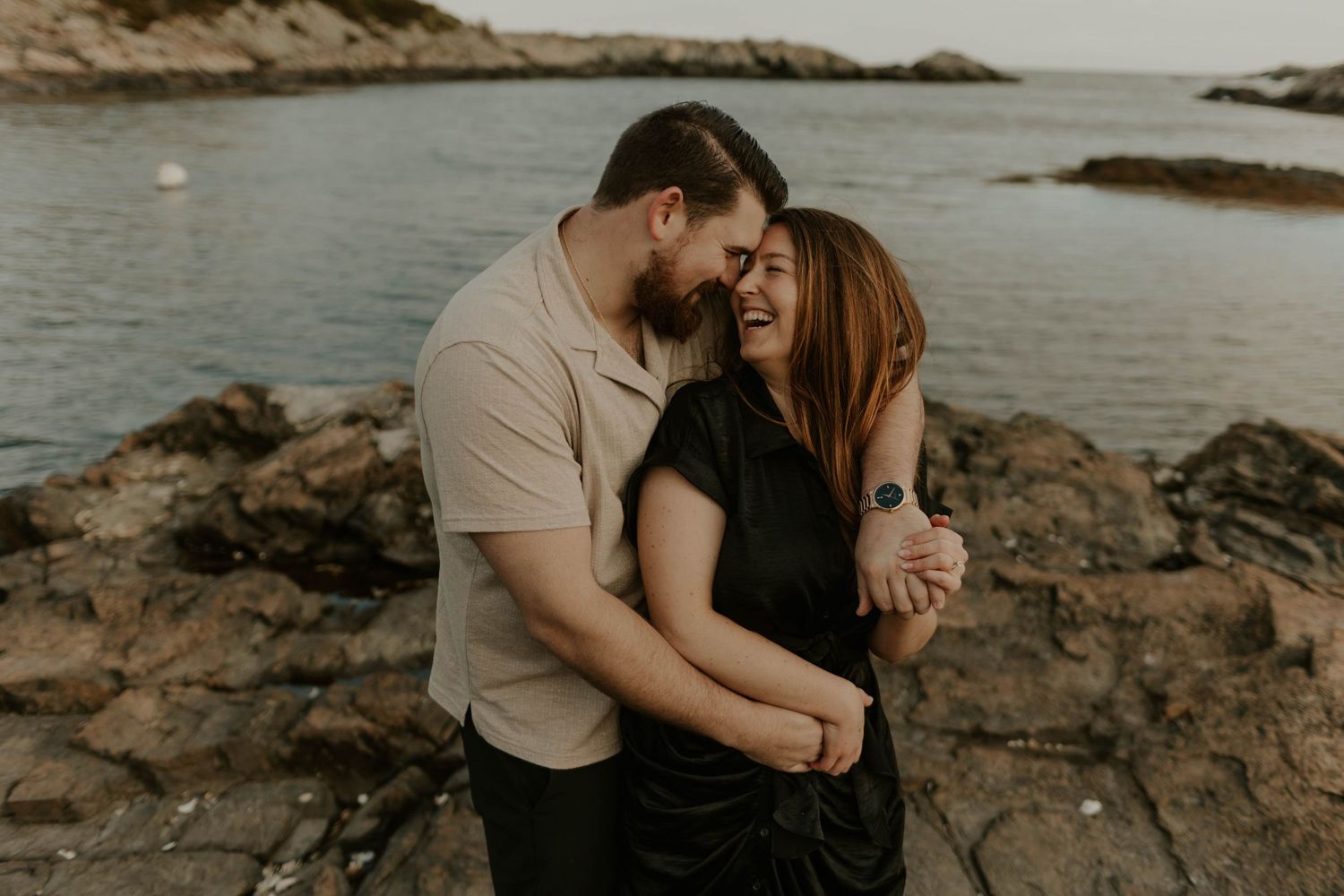 A romantic couple embracing on rocky coastal cliffs during golden hour.