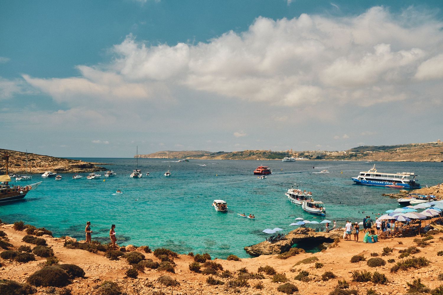 Boats floating in vibrant turquoise Mediterranean waters surrounded by rocky coastline under blue skies.