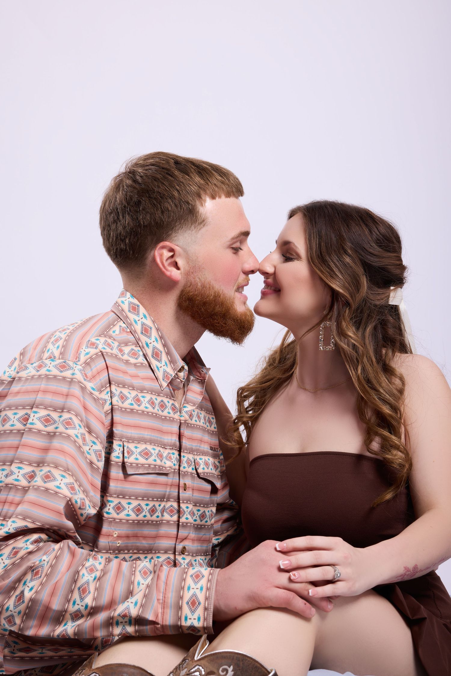 Intimate couple sharing a tender moment in casual attire against light background during romantic photo shoot.