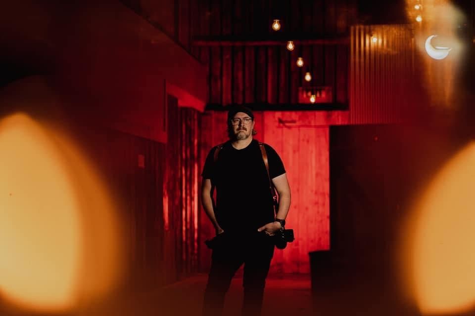 Moody portrait of photographer in black against red lighting and dark atmosphere.