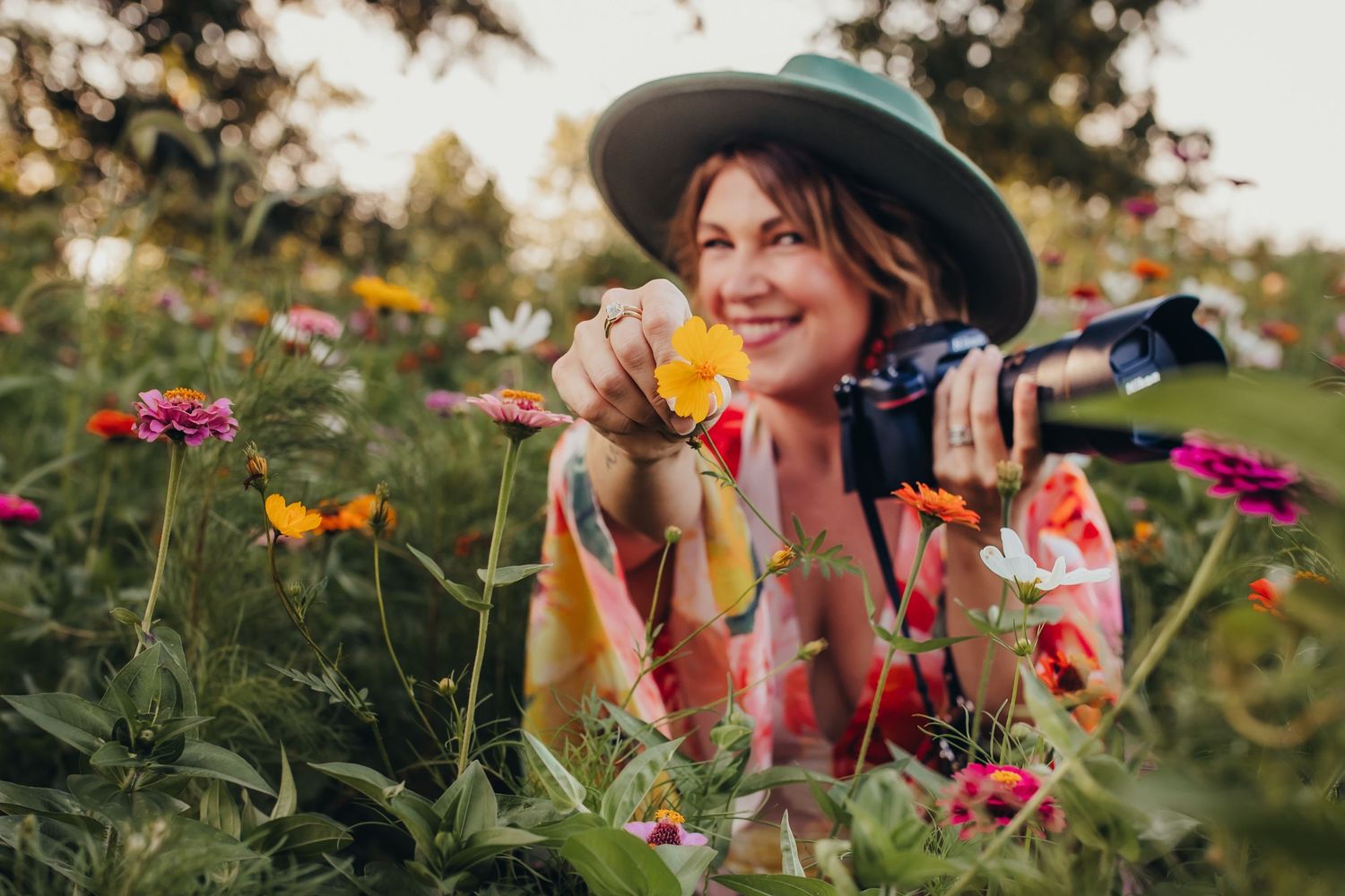 Gardener in wide brim hat exploring colorful flower garden with camera.