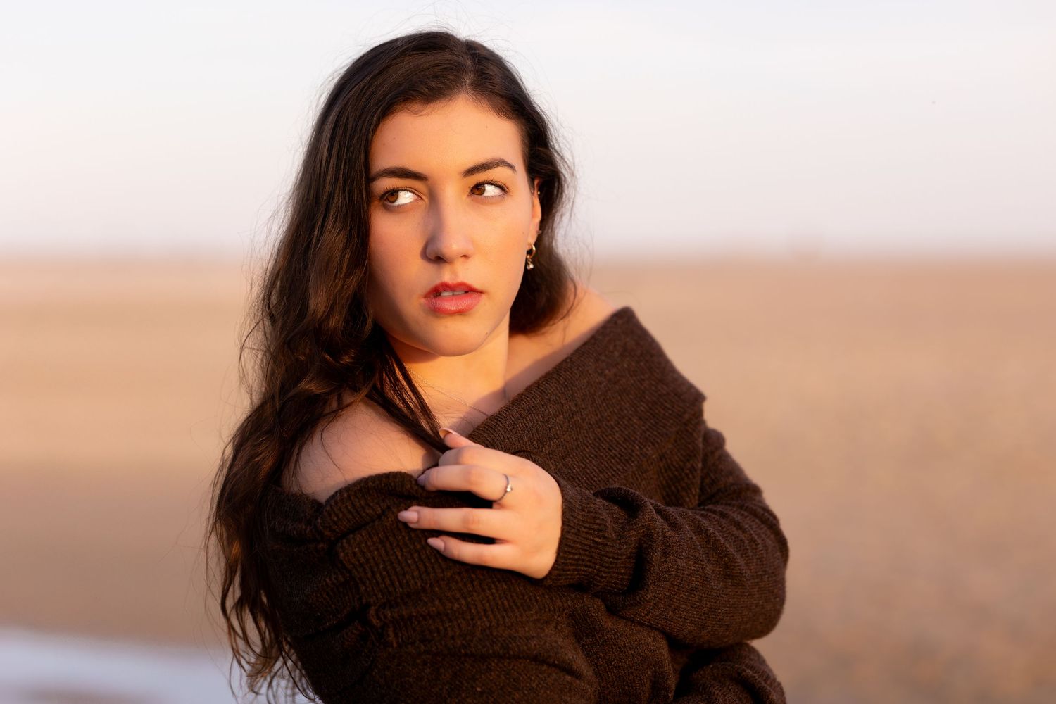 A woman with dark hair poses outdoors at sunset wearing a black top and natural makeup.