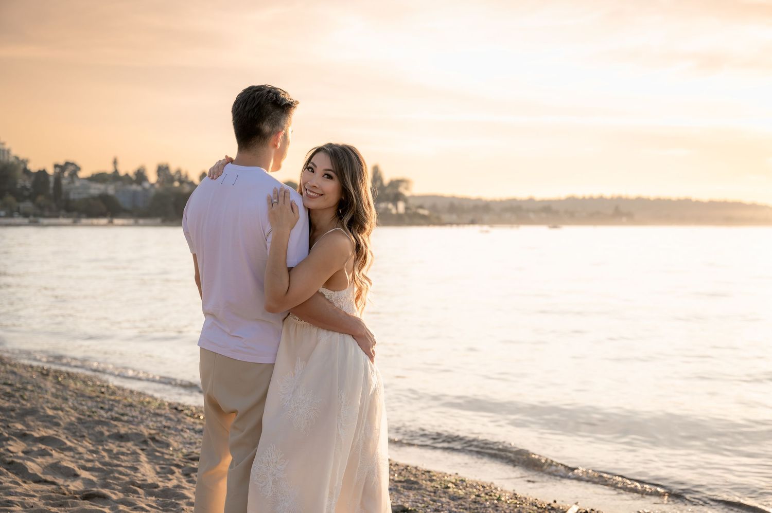 A romantic sunset beach portrait of a couple embracing on golden sand with ocean views in the background.