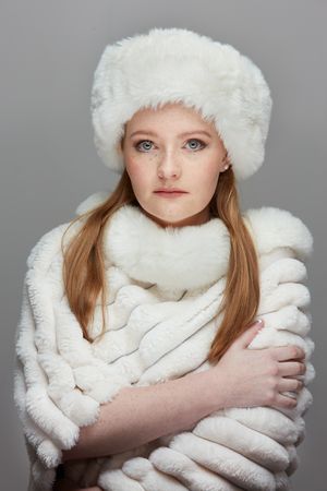 A series of photos showing someone wearing a white fluffy winter hat and scarf against a gray background.