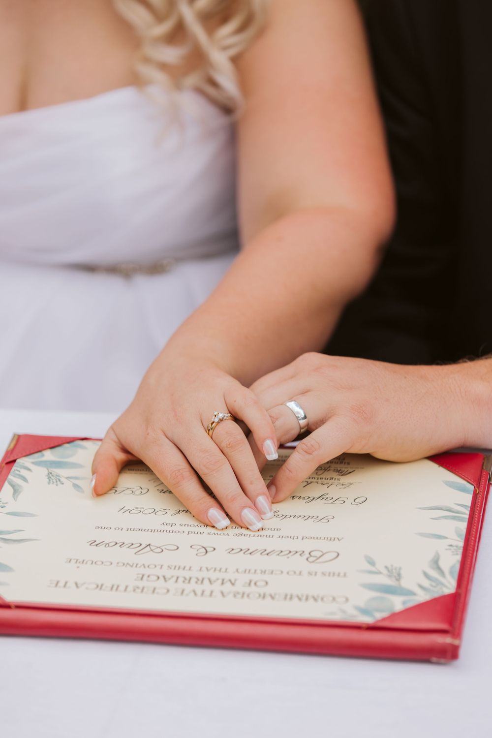 Close-up of hands signing a wedding certificate with red border details.