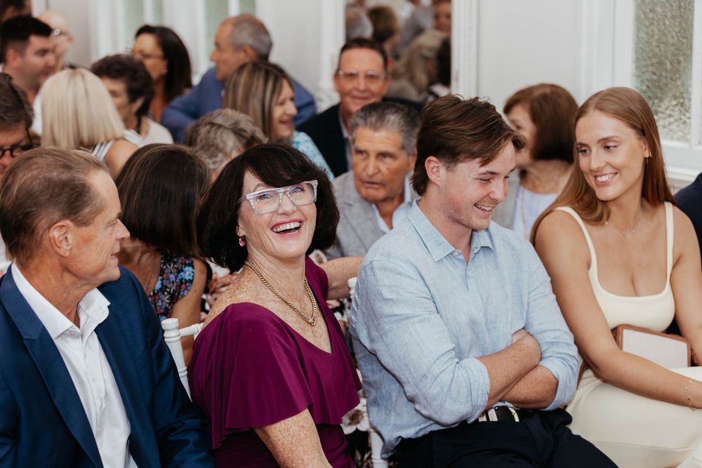Wedding guests smile and laugh during an indoor reception celebration.