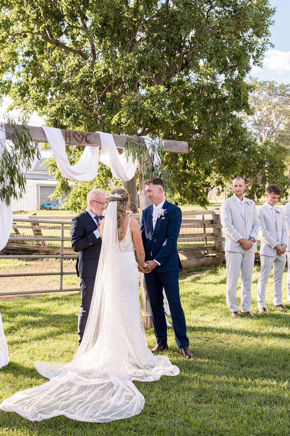 Wedding ceremony on a grassy lawn with white fabric decorations and trees in the background.