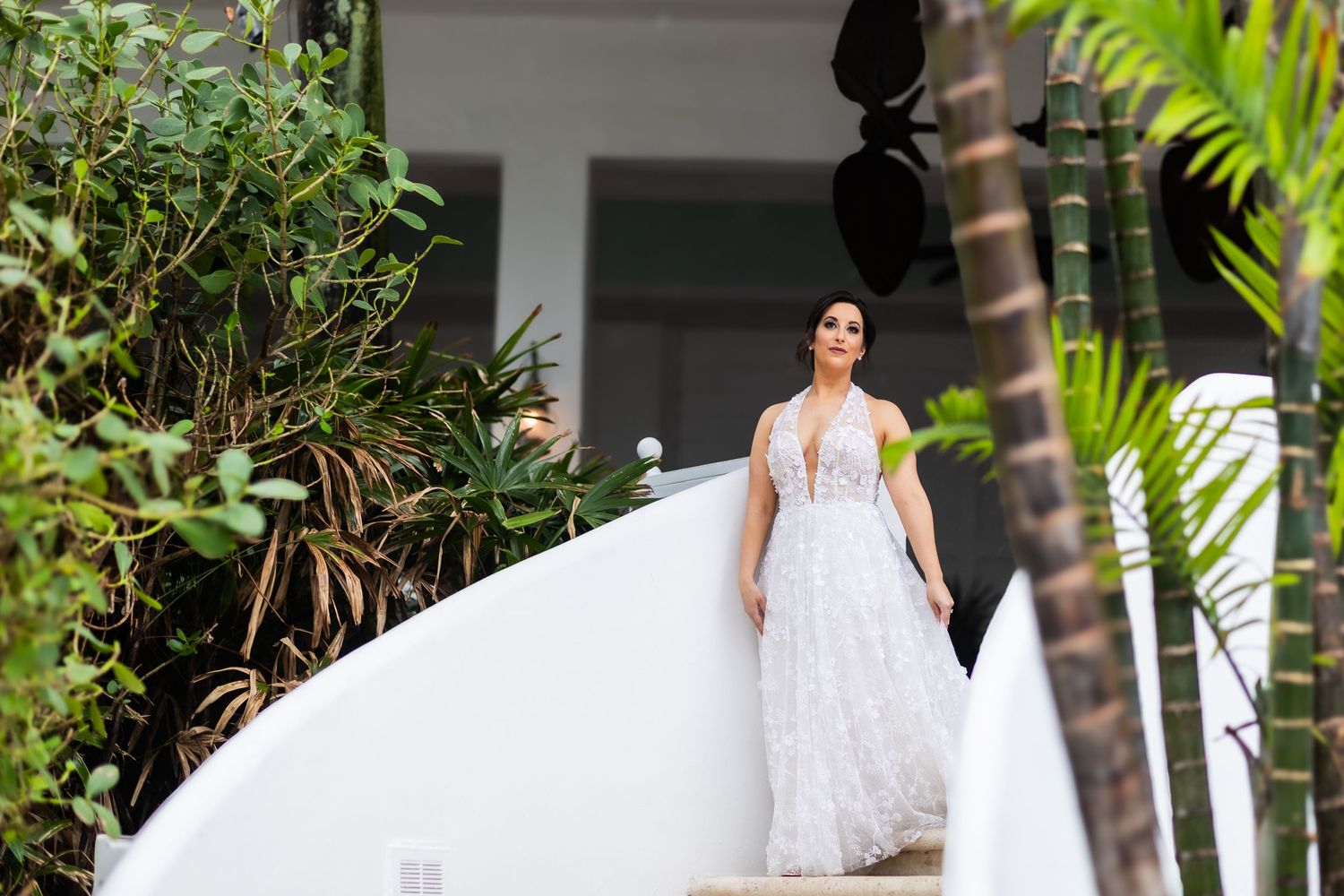 Classic wedding portrait on white colonial-style porch surrounded by lush tropical plants.