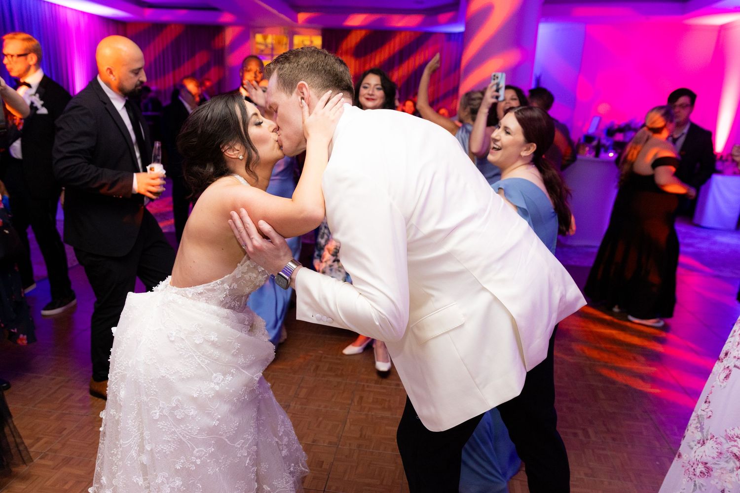 Wedding reception guests dancing under colorful purple and pink lighting.