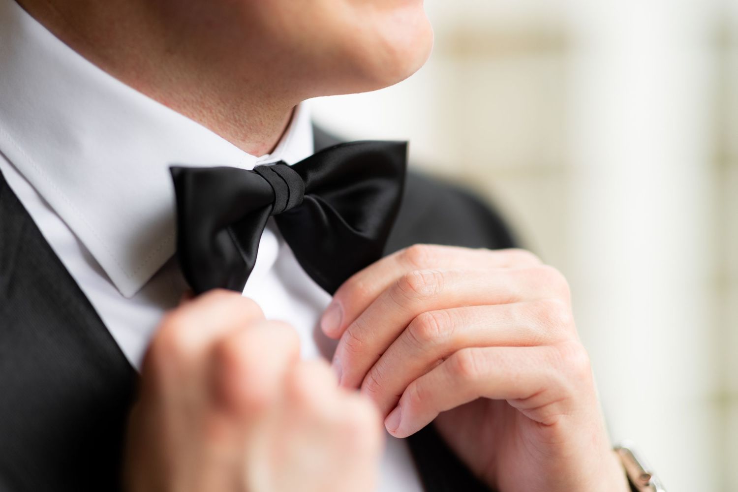 Detail shot of groom adjusting black bow tie with white shirt.