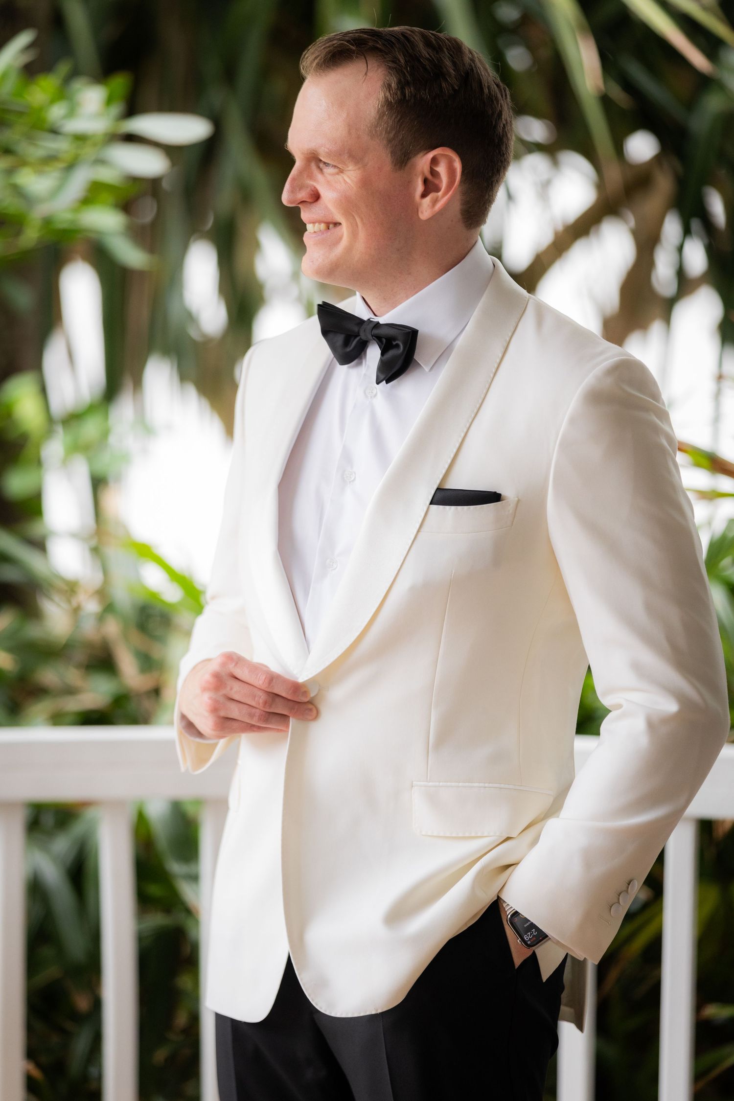 Candid portrait series of groom in white tuxedo jacket on tropical porch.