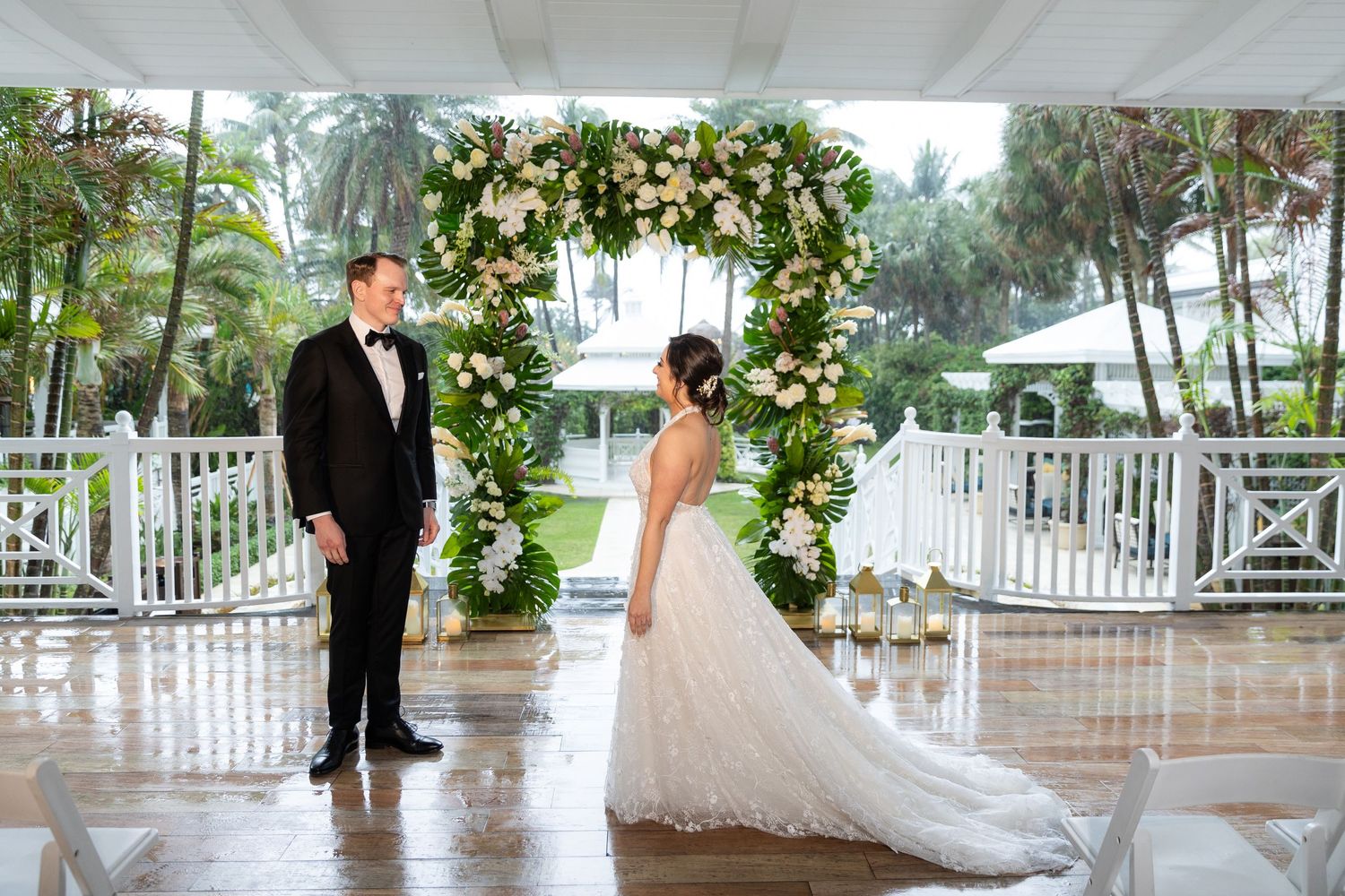 Elegant outdoor wedding venue with white floral arch and covered patio during rainfall.