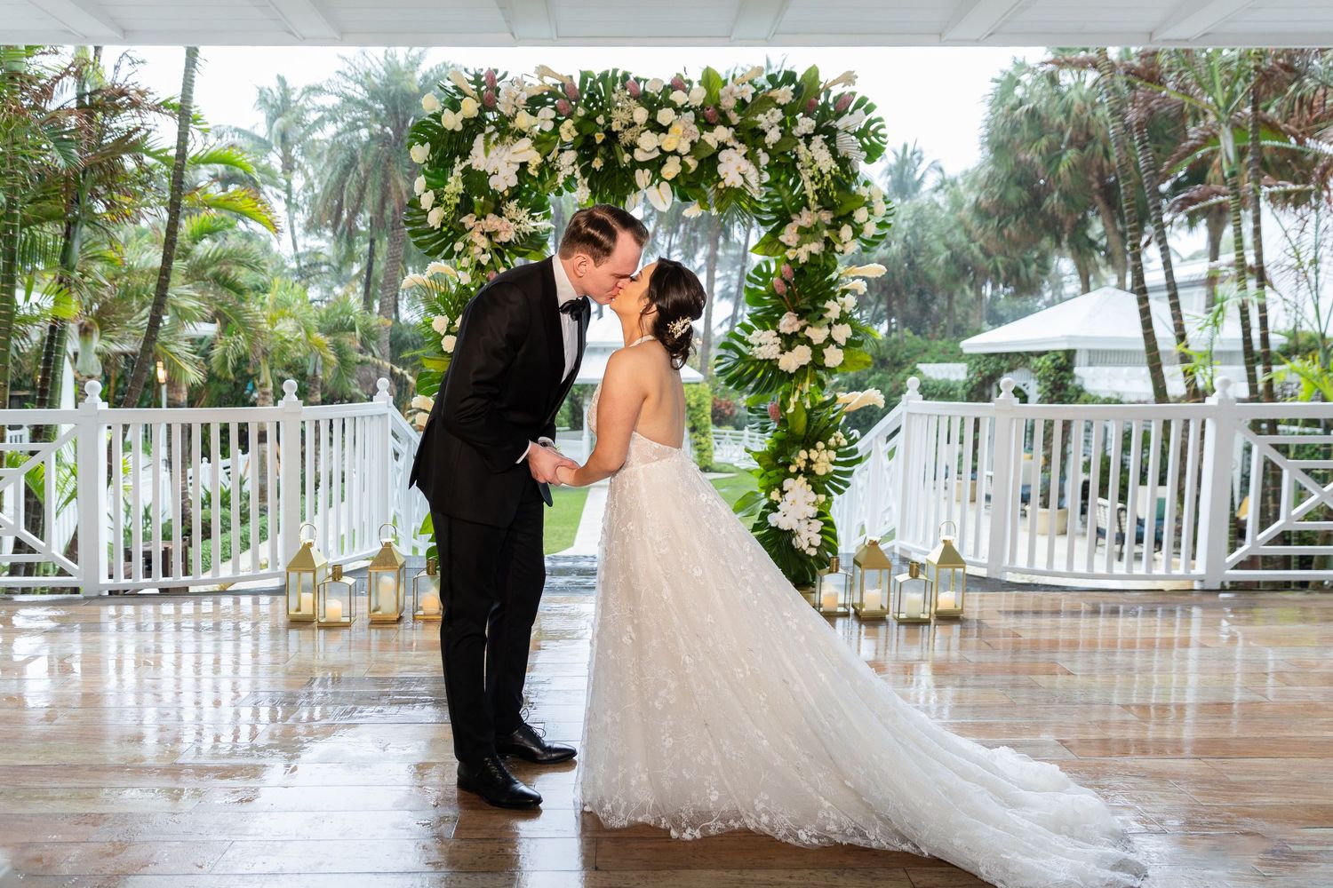 Wedding couple shares first look moment under floral arch on rainy covered porch.