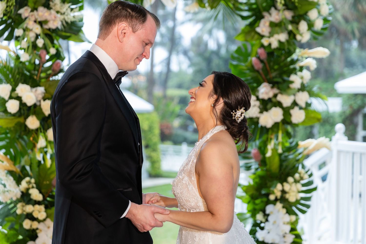 Wedding couple shares emotional moment beneath ornate white floral installation on covered porch.