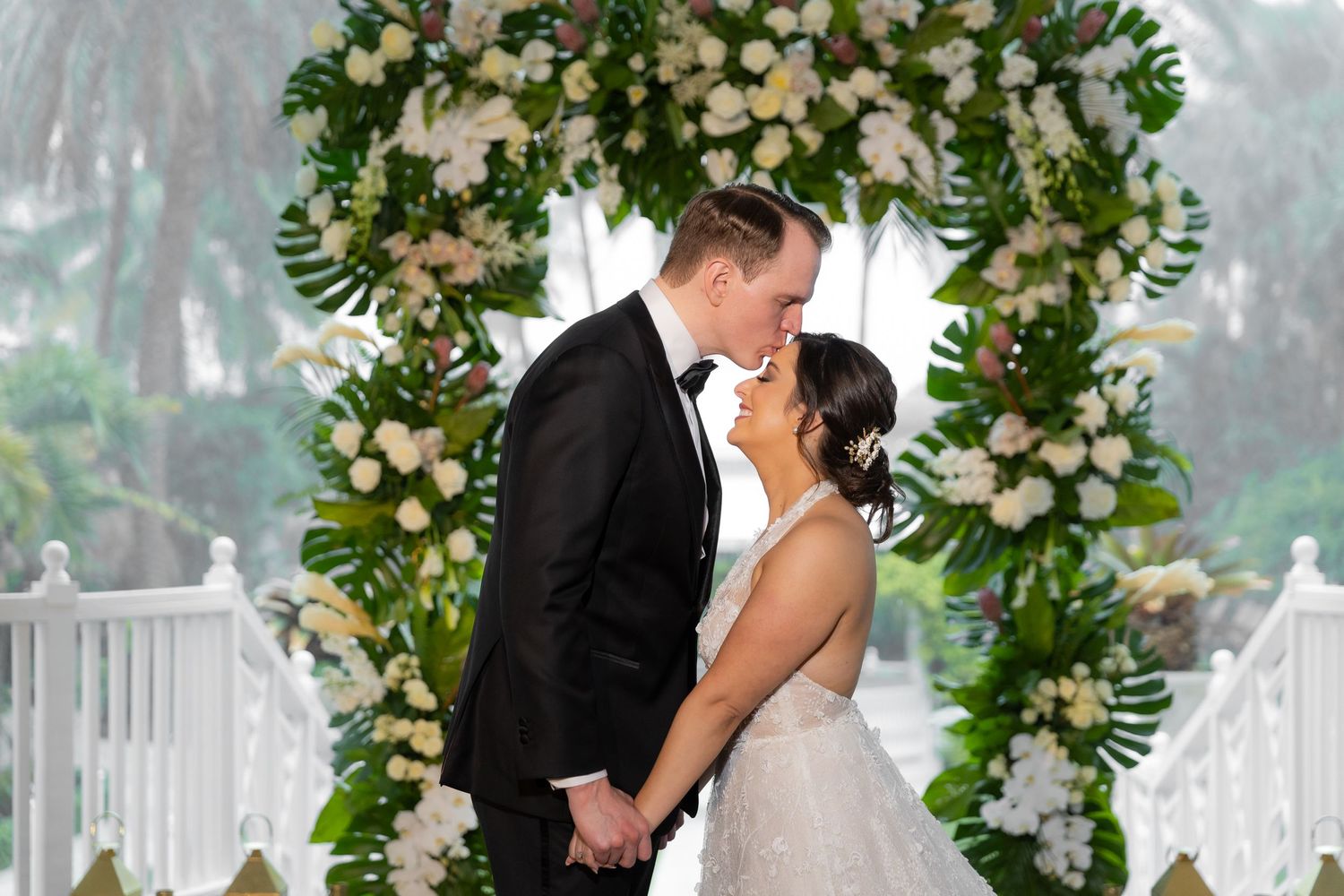 Couple celebrates during wedding ceremony beneath elegant white and green floral installation.