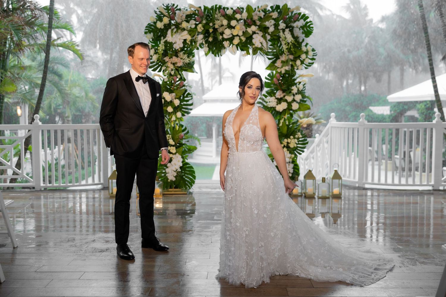 A rainy wedding day photo with a couple walking under a floral arch on a porch.
