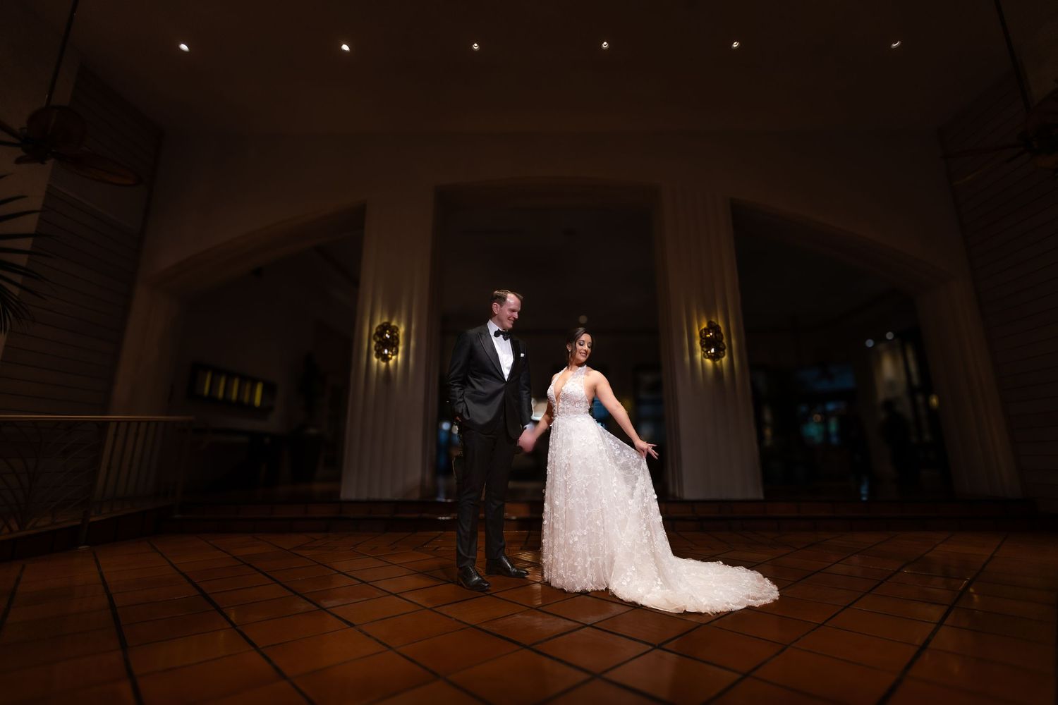 Elegant wedding couple posing in a grand ballroom with ornate lighting.