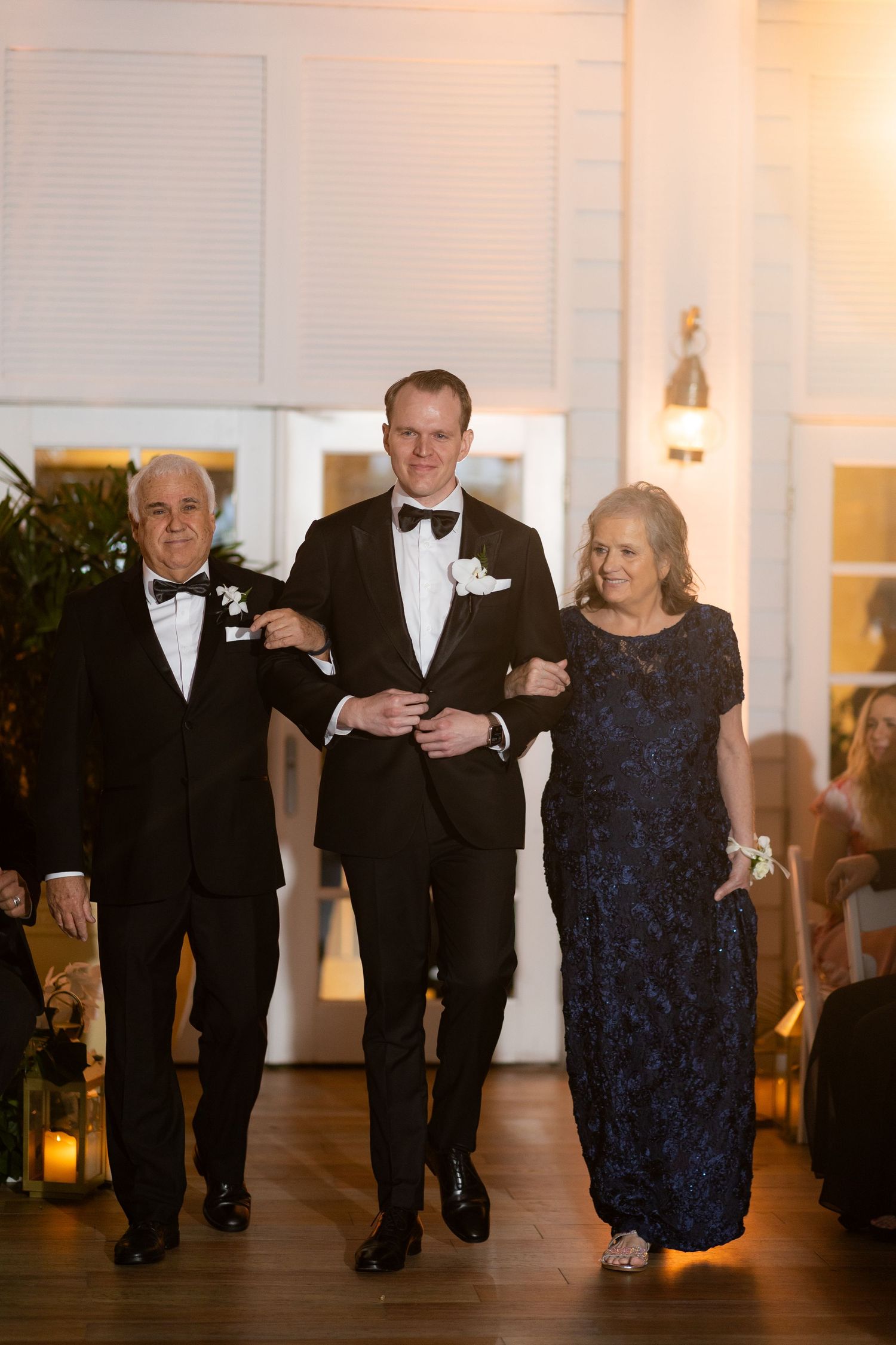 Wedding party members in formal attire walk down the aisle together.