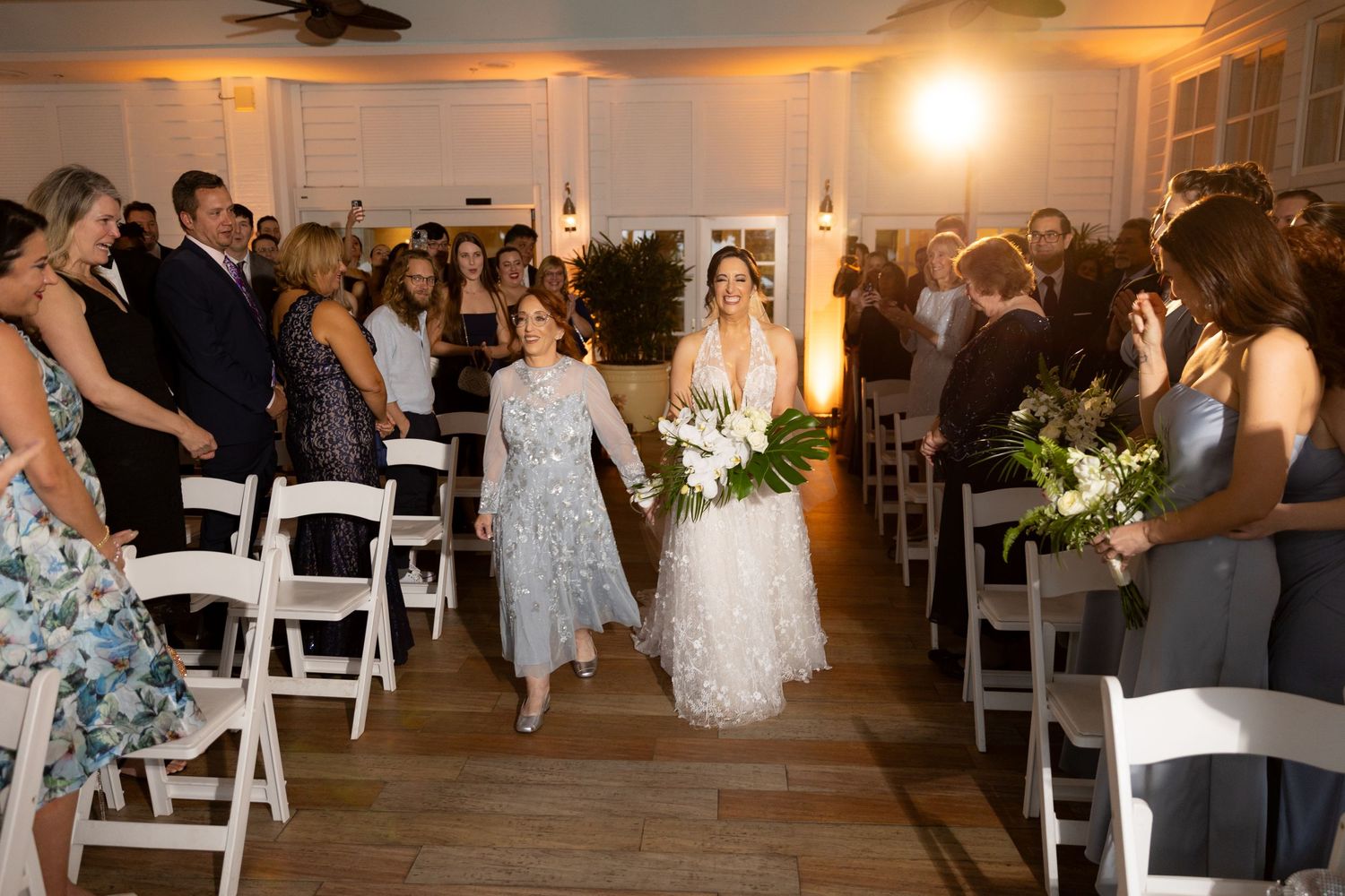Wedding celebration in a warmly lit reception hall with white folding chairs.