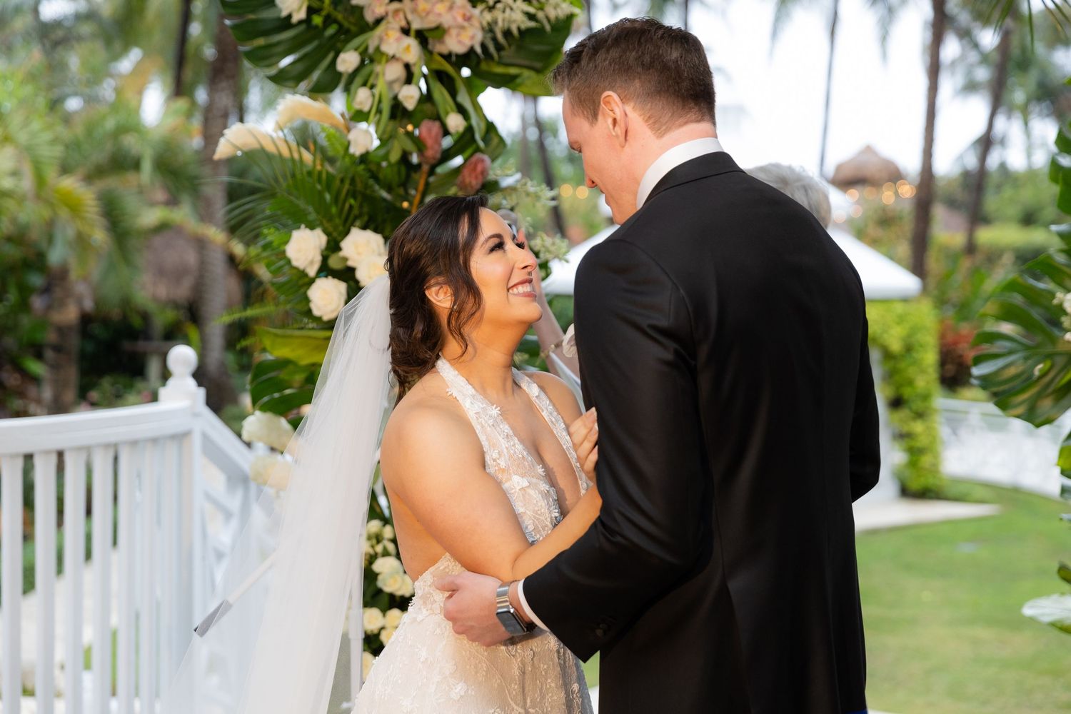 Garden wedding ceremony with palm trees and white gazebo in the background.