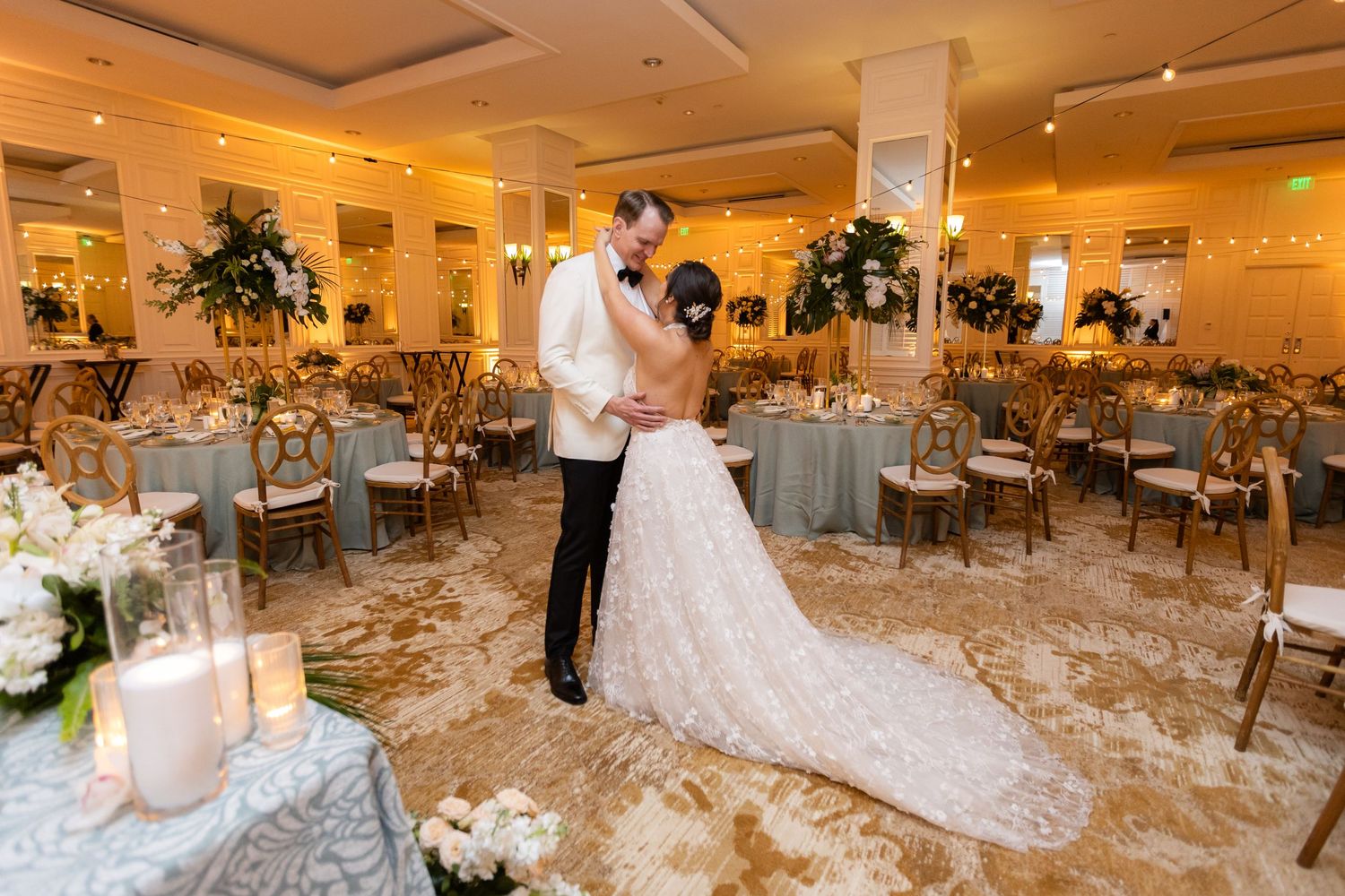 Elegant wedding reception hall set with round tables and white linens in warm lighting.