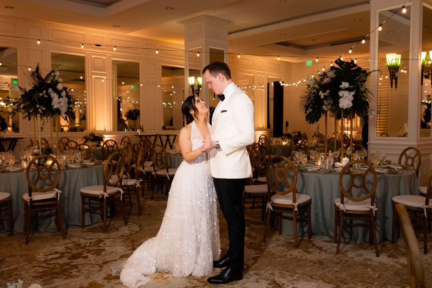 Large ballroom decorated for a wedding reception with multiple round tables and elegant lighting.