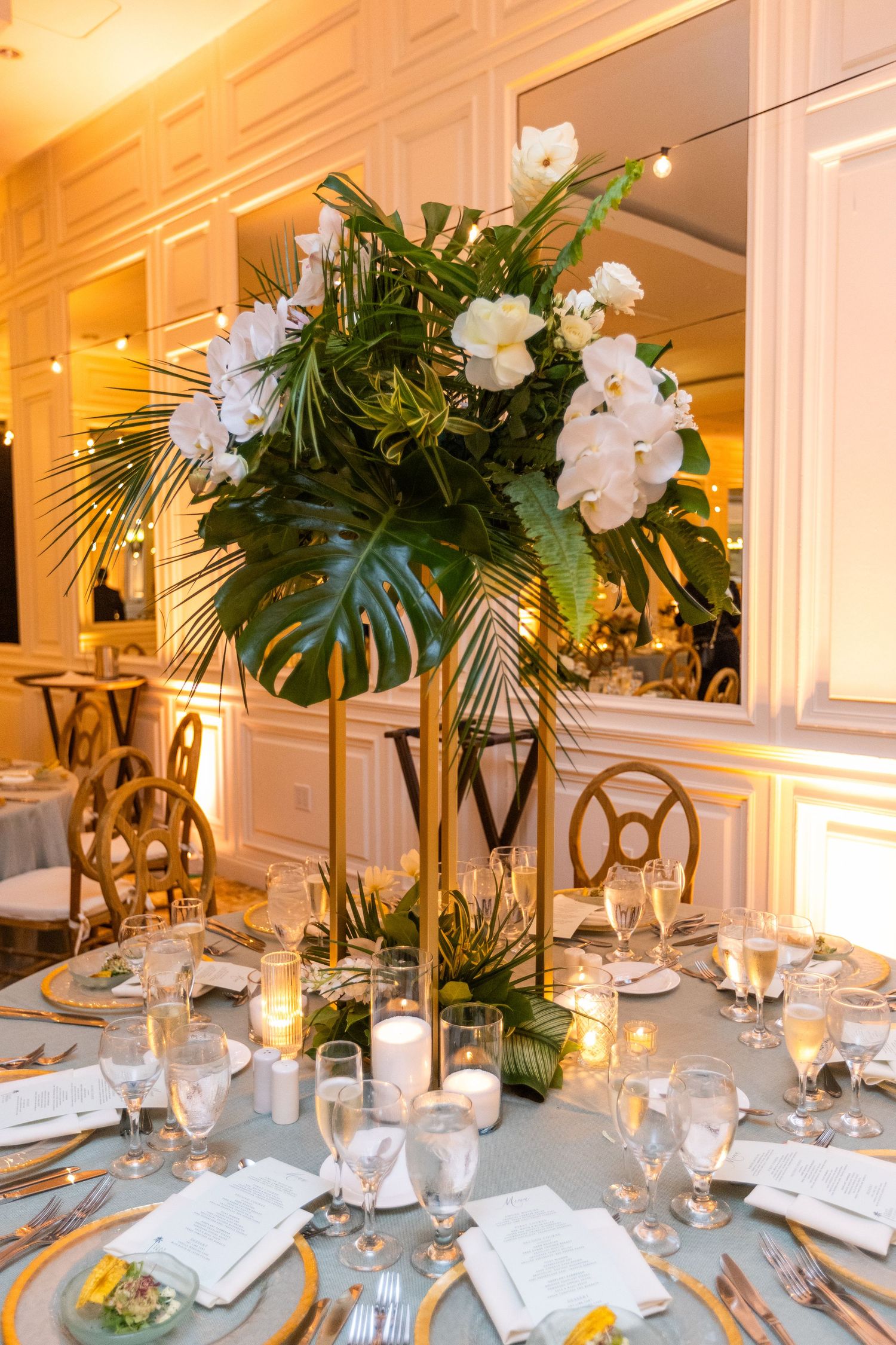Tropical-themed wedding centerpieces with palm leaves and white orchids on elegantly set tables.