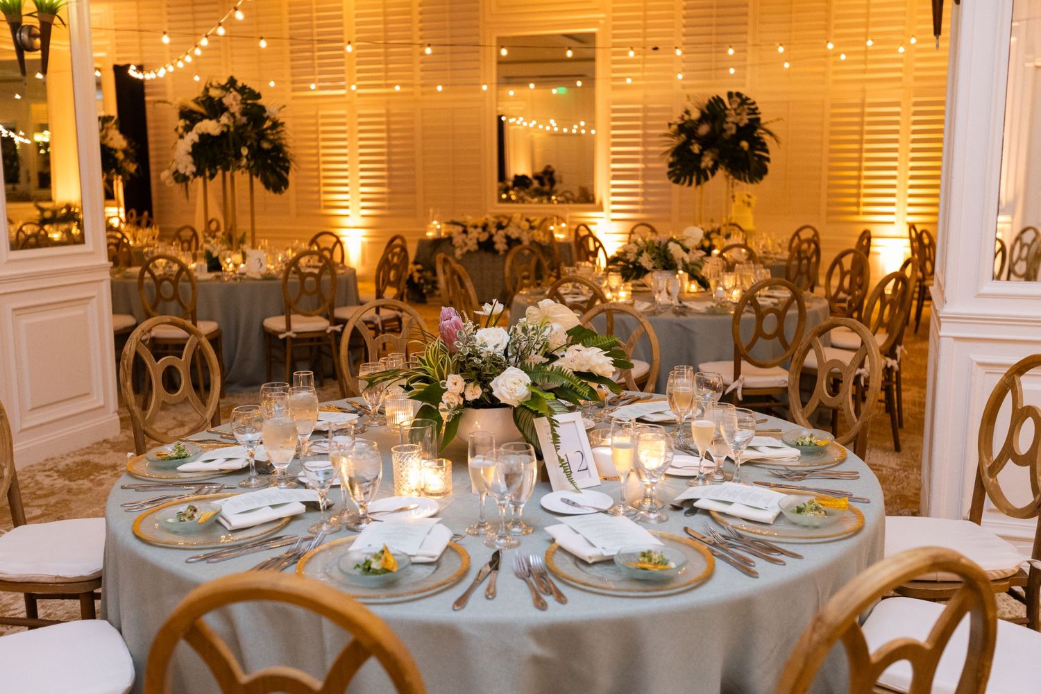 Wedding reception room with string lights and round tables decorated in white and gold accents.