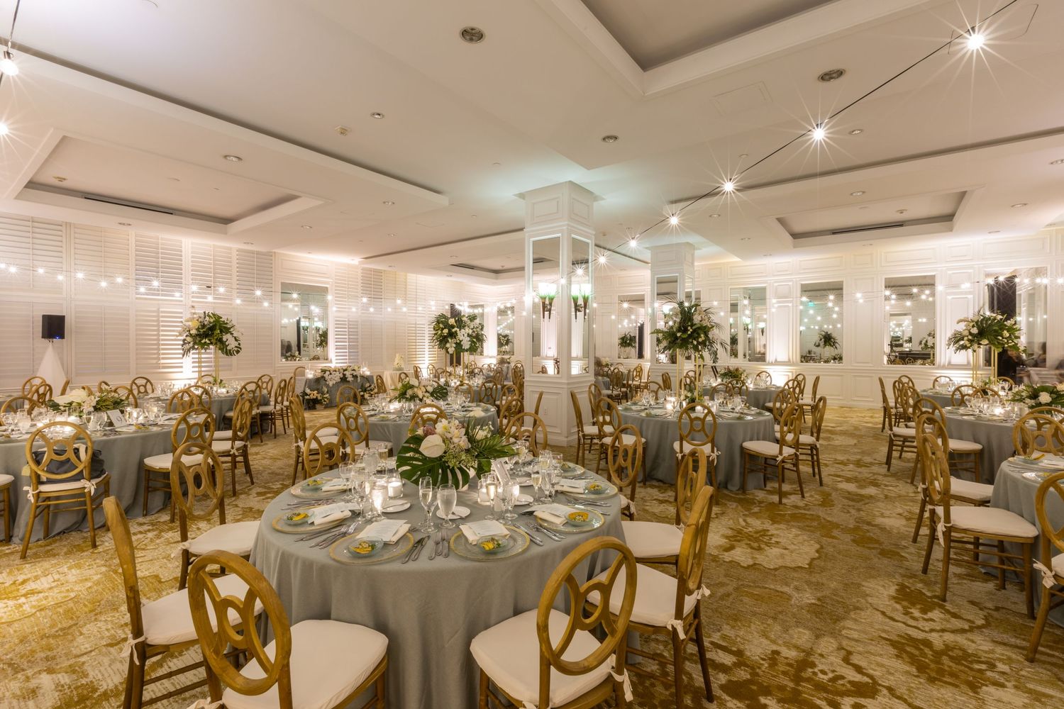 Spacious wedding venue with multiple round tables and wooden chairs set for celebration.