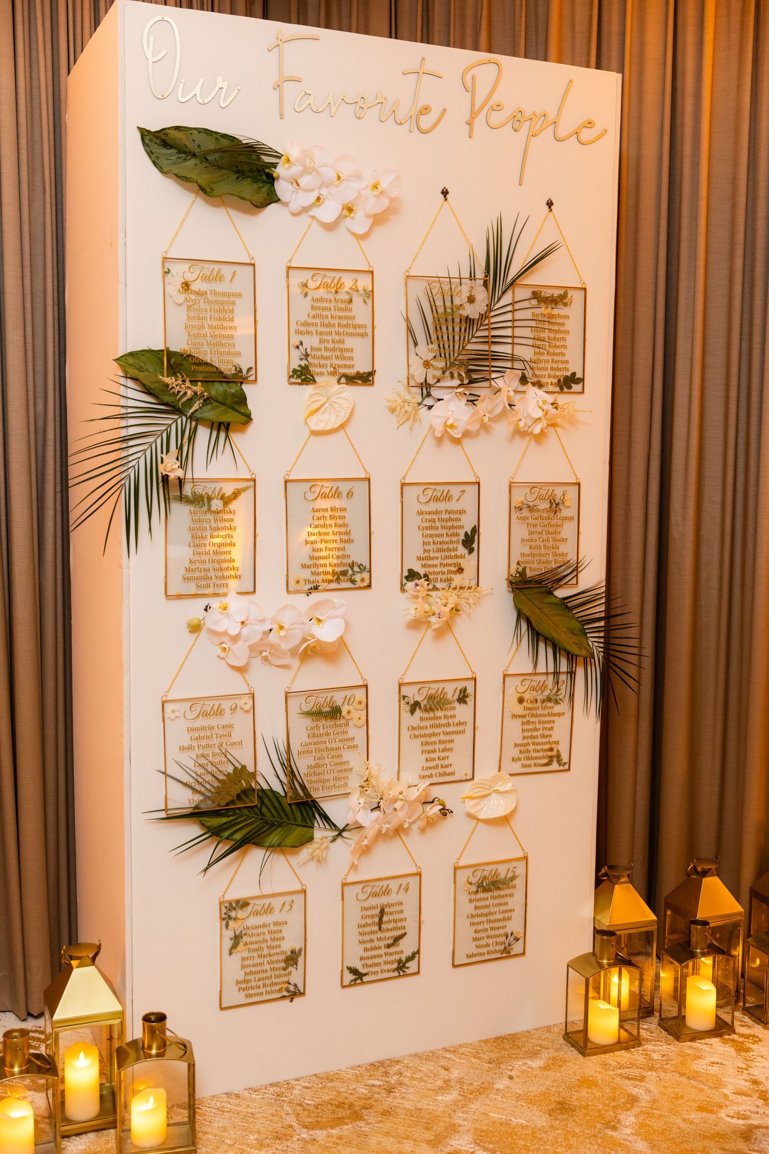 Wedding seating chart display decorated with tropical leaves and illuminated by candlelight.