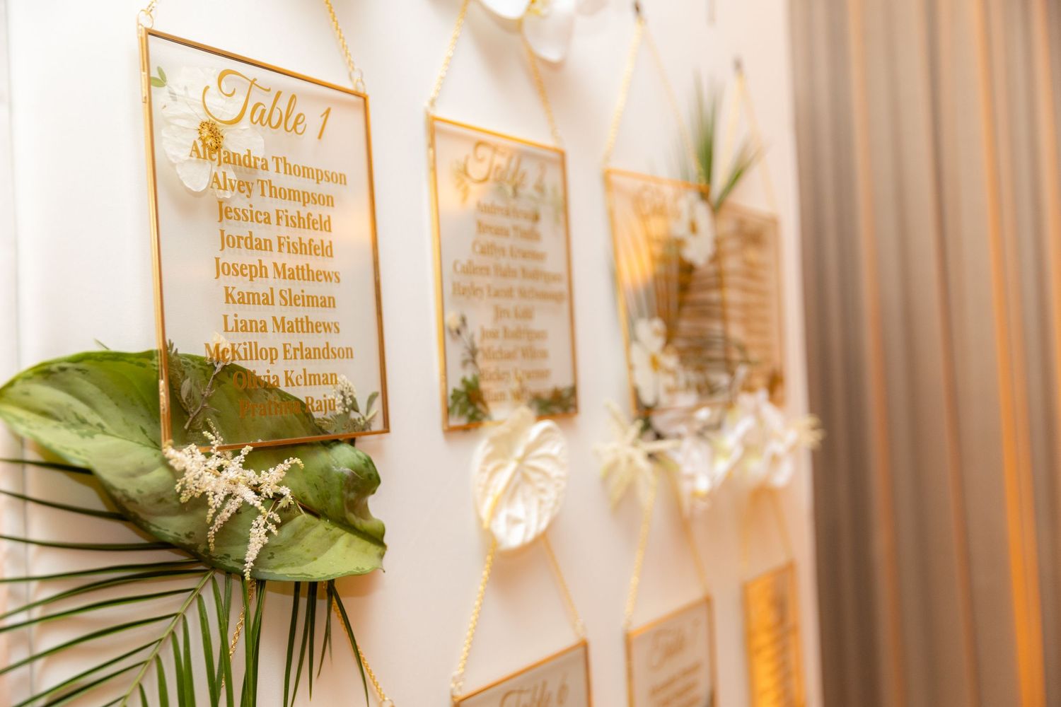 Detail shot of wedding seating arrangements displayed on white boards with palm leaf accents.