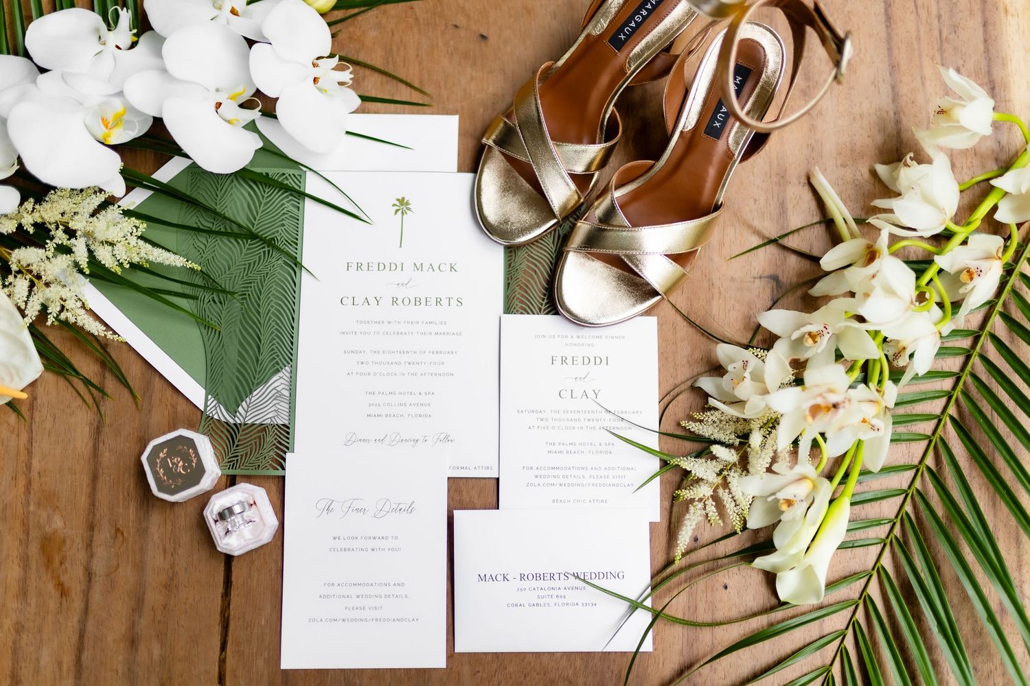 Wedding invitation suite with white flowers and greenery arranged on wooden surface with elegant paper details.
