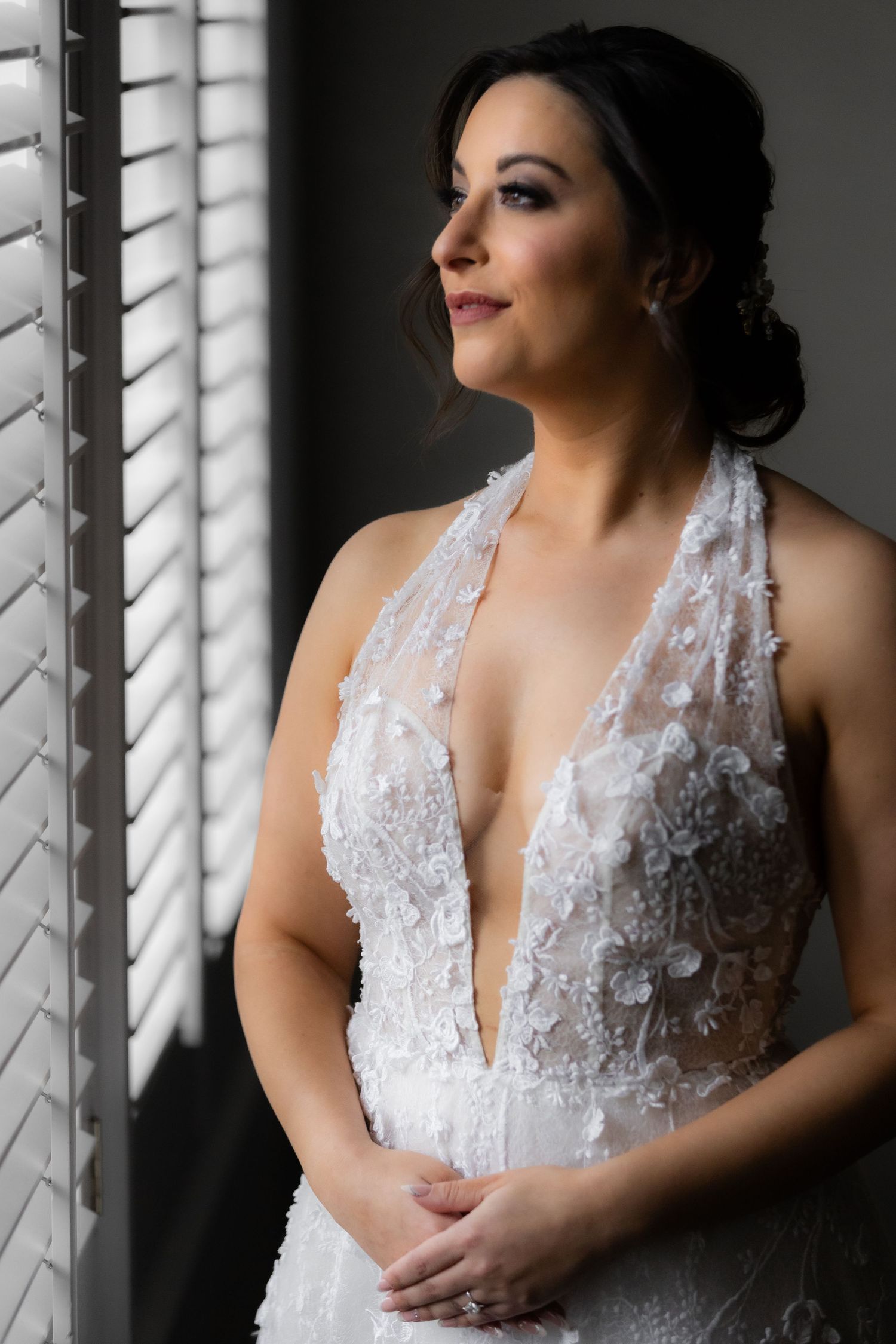 Wedding dress detail shot through window blinds creating dramatic lighting and shadows.