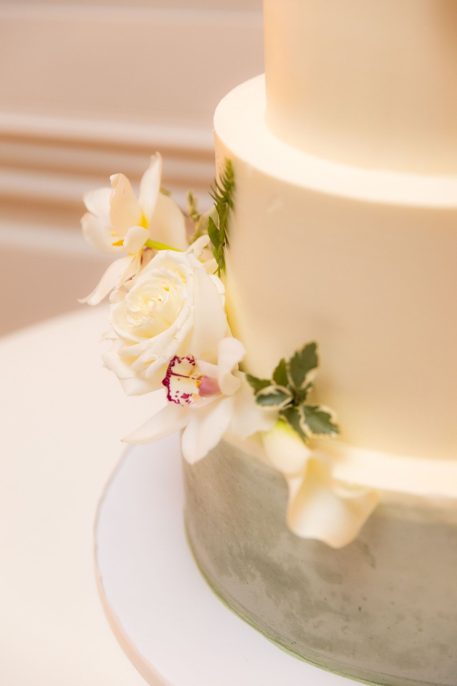 Close-up detail of a white wedding cake decorated with delicate orchids and green foliage.