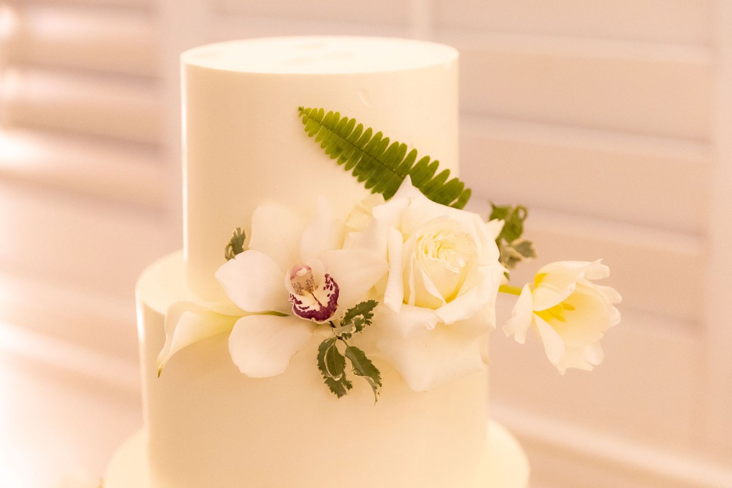 Elegant white wedding cake with orchid decorations photographed from the side.