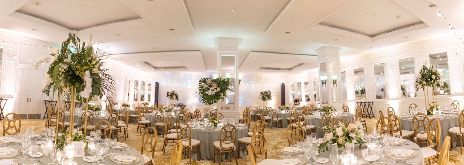 Panoramic view of an elegant wedding reception ballroom with round tables and decorative lighting.