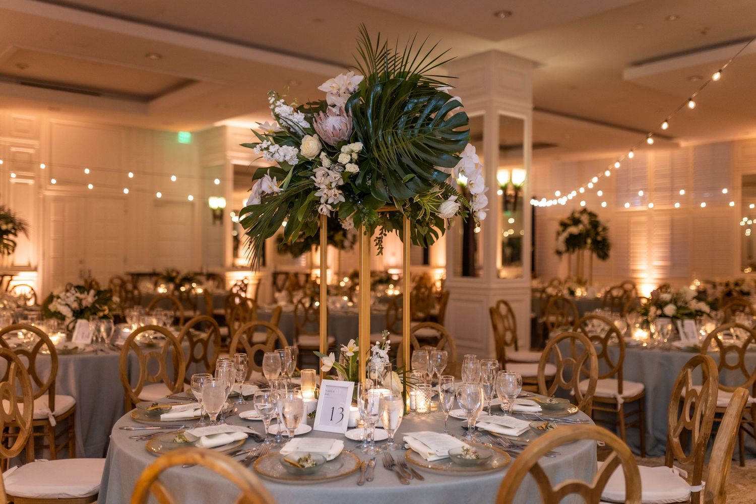Wide shot of a luxurious wedding reception hall with elegant table settings and string lights.
