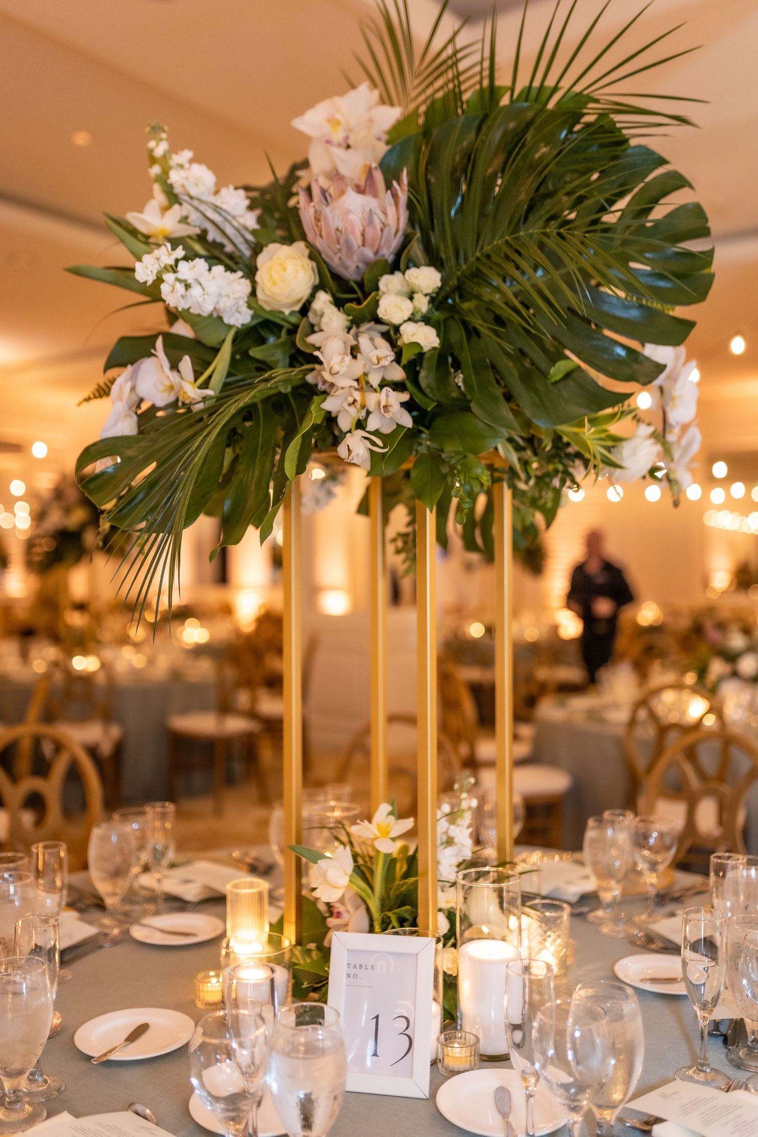 Tropical-themed wedding centerpieces with monstera leaves and white flowers on reception tables.