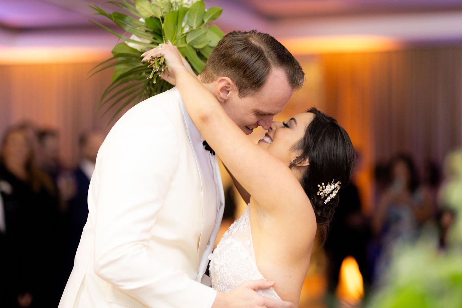Newlyweds share their first dance on an illuminated ballroom floor surrounded by wedding guests.