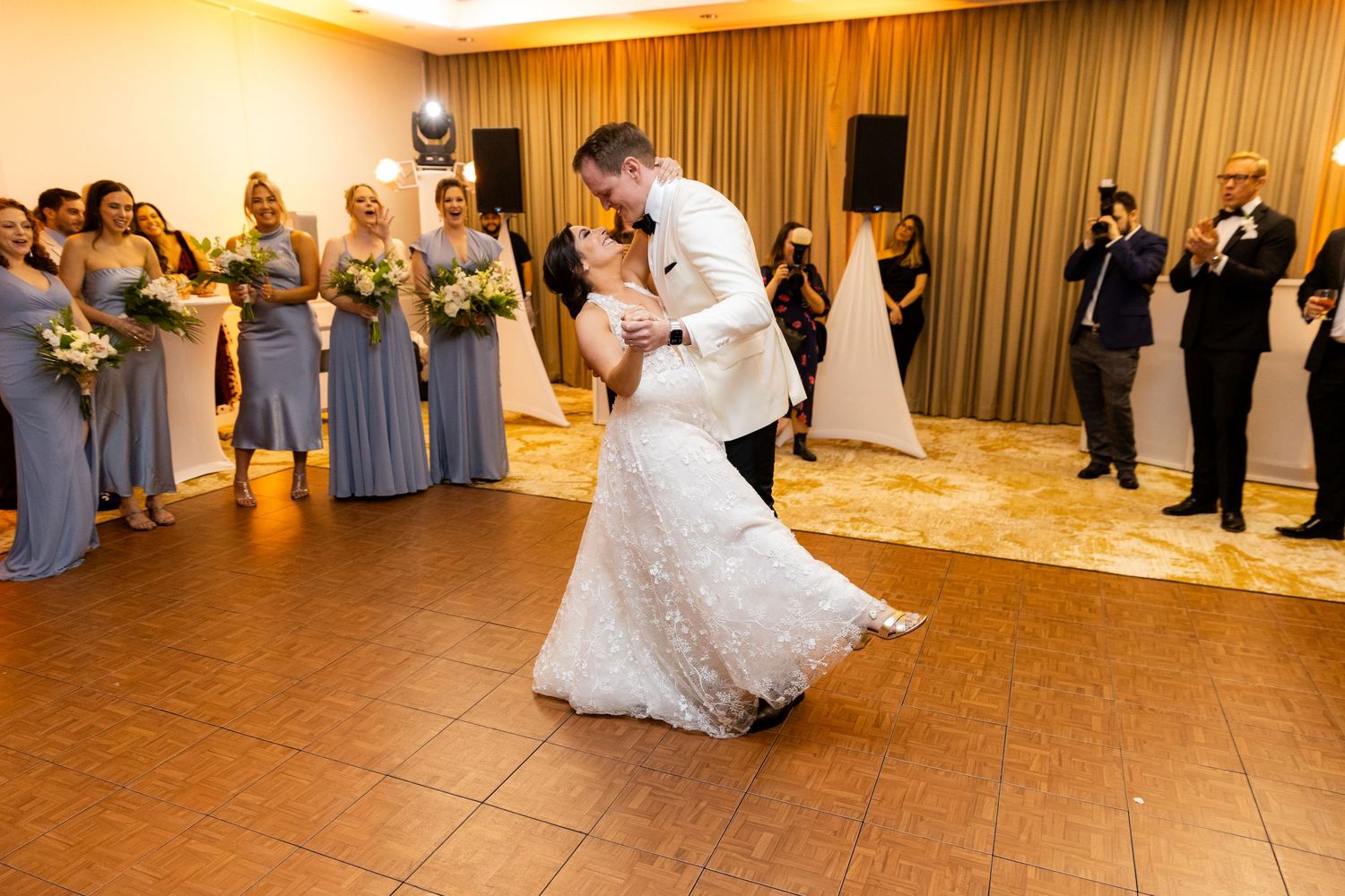 Wedding guests watching as couple performs choreographed dance routine on reception floor.